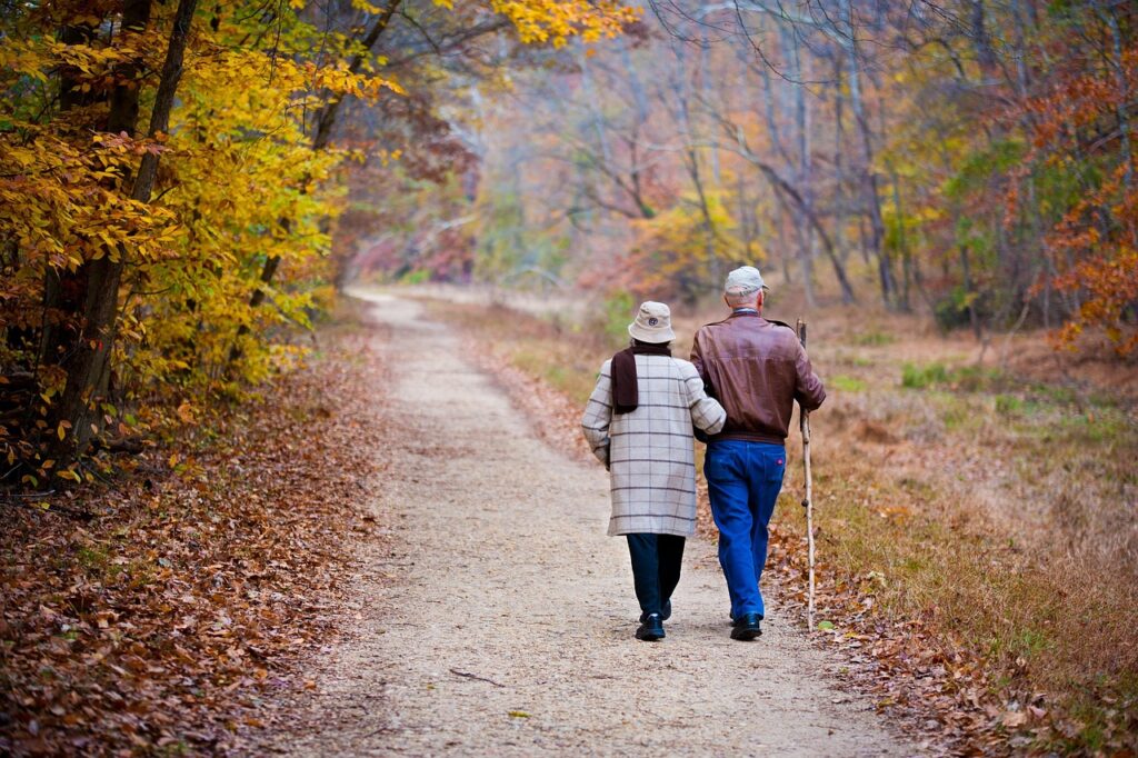 Older couple walking arm in arm along a leafy autumn trail