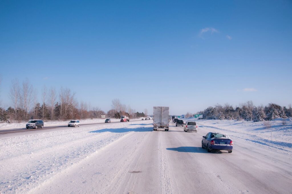 Cars and a truck driving on a snow-covered highway under a clear sky