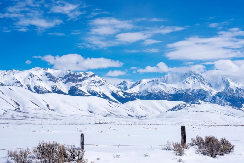 Snow-covered mountain range behind a wide snowy valley and fence line